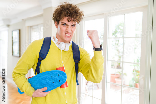 Young student man wearing headphones and backpack holding skateboard annoyed and frustrated shouting with anger, crazy and yelling with raised hand, anger concept © Krakenimages.com