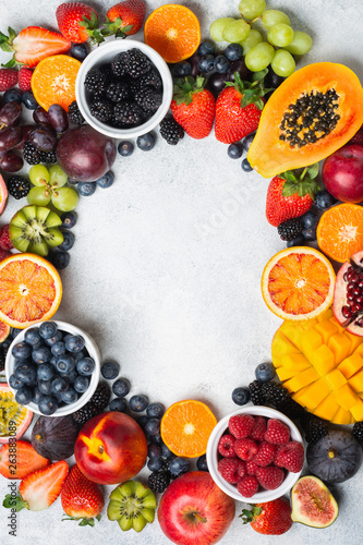 Frame made of healthy raw fruits, mango papaya strawberries oranges passion fruits berries on oval serving plate on light concrete background, top view, copy space, selective focus