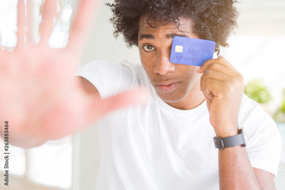 African American man holding credit card with open hand doing stop sign with serious and confident expression, defense gesture African American man holding credit card with open hand doing stop sign with serious and confident expression, defense gesture