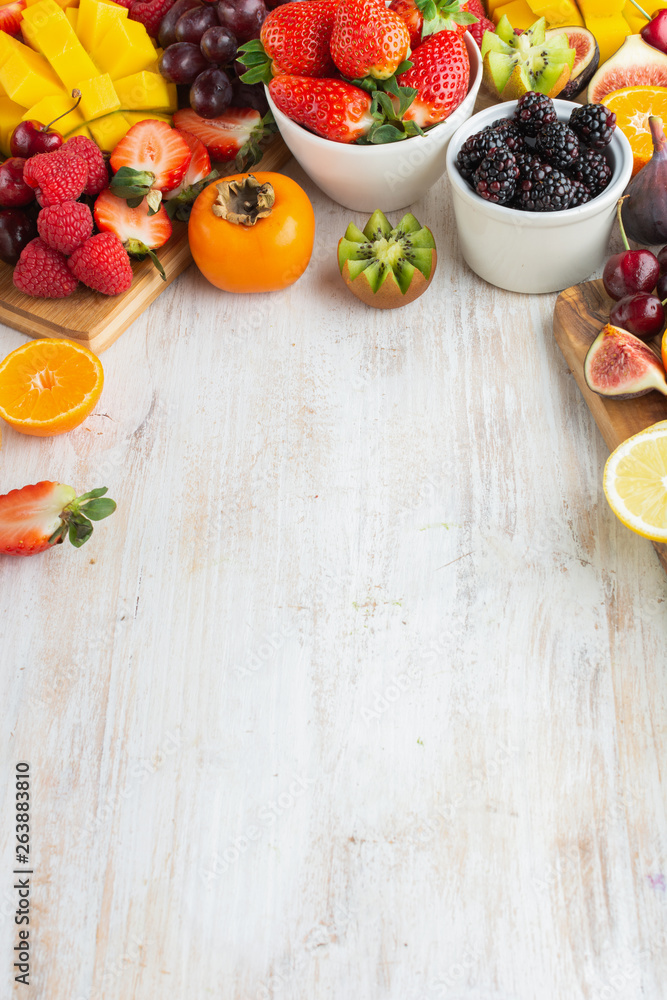 Healthy raw fruits background, cut mango, strawberries raspberries oranges plums apples kiwis grapes blueberries cherries, on white table, copy space, top view, selective focus Healthy raw fruits background, cut mango, strawberries raspberries oranges plums apples kiwis grapes blueberries cherries, on white table, copy space, top view, selective focus