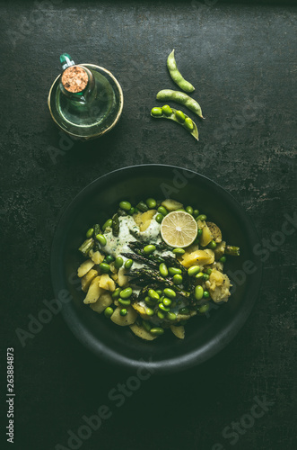 Green potatoes salad with roasted green asparagus, edamame soybeans, lime and green peas on dark rustic kitchen table background, top view. Copy space. Healthy vegetarian food .