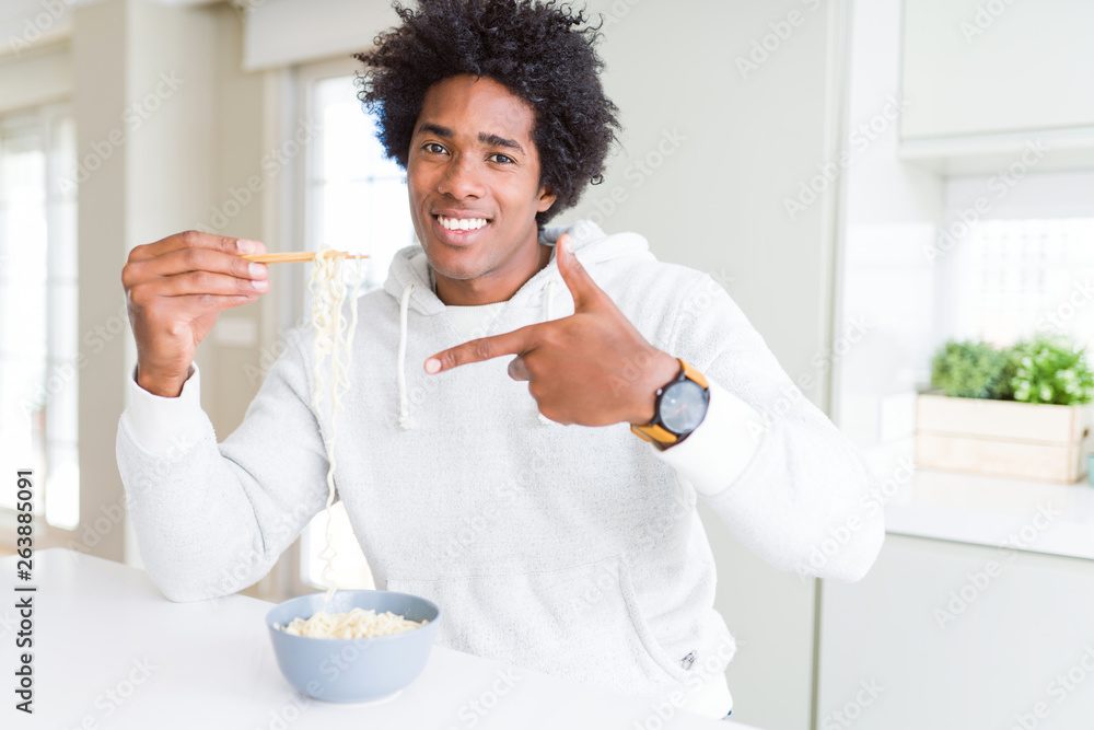 African American man eating asian noodles using chopsticks at home very happy pointing with hand and finger African American man eating asian noodles using chopsticks at home very happy pointing with hand and finger