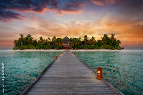 Holzsteg führt zu einer tropischen Paradiesinsel mit Palmen und Sandstrand bei Sonnenuntergang, Malediven, Indischer Ozean