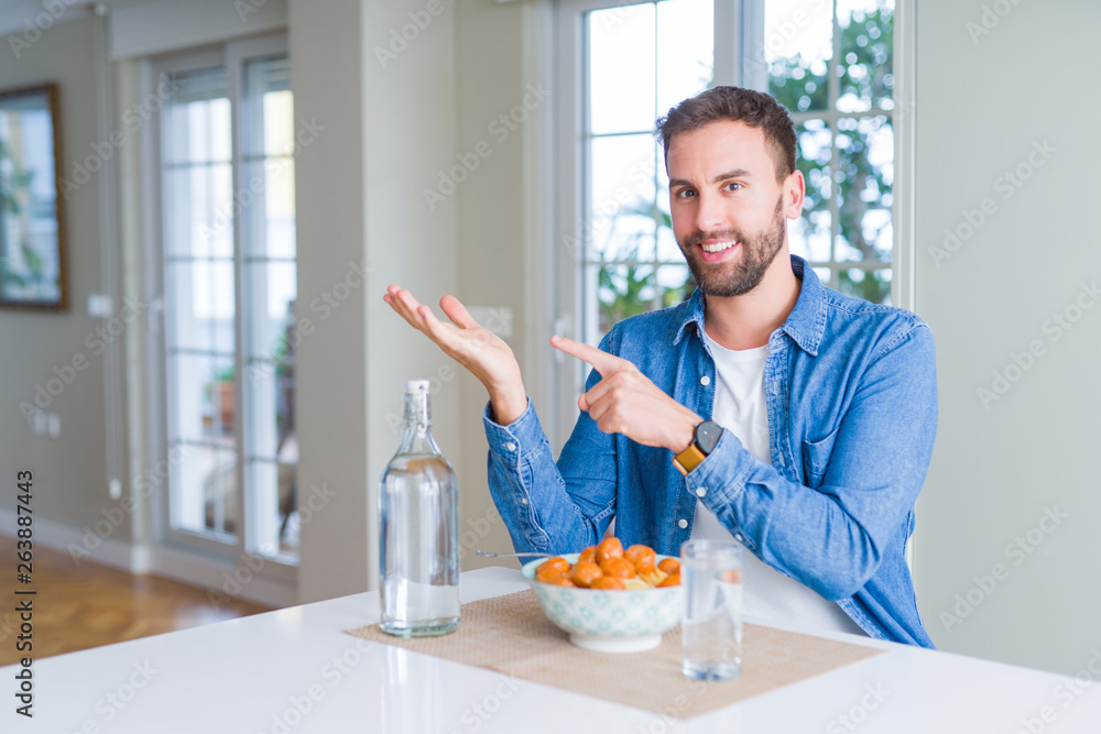 Handsome man eating pasta with meatballs and tomato sauce at home amazed and smiling to the camera while presenting with hand and pointing with finger. Handsome man eating pasta with meatballs and tomato sauce at home amazed and smiling to the camera while presenting with hand and pointing with finger.