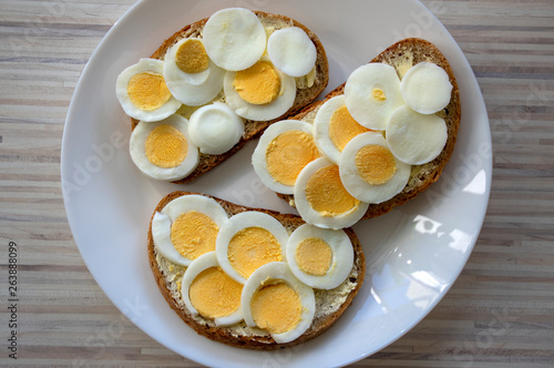 Sliced hard boiled eggs on common czech bread with butter on white plate on light wooden table