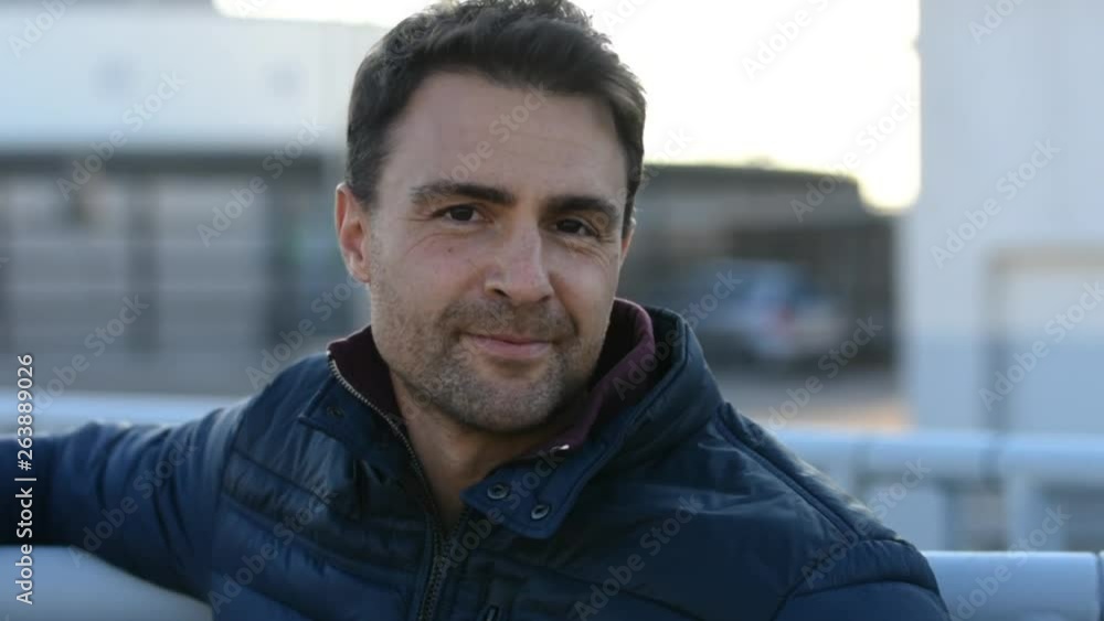 Man on a coat resting his arm on a railing turning his head and smiling. Man on a coat resting his arm on a railing turning his head and smiling.