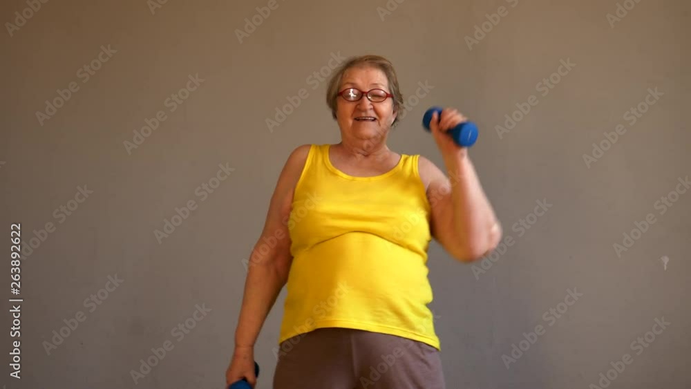 Elderly woman grandmother in yellow shirt doing gymnastics with dumbbells Elderly woman grandmother in yellow shirt doing gymnastics with dumbbells
