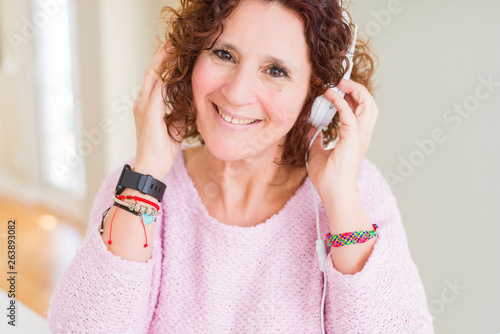 Senior woman wearing headphones listening to music with a happy face standing and smiling with a confident smile showing teeth photo