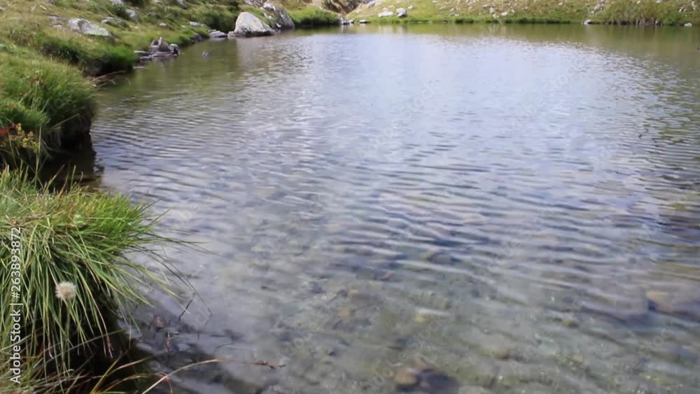 Camera movement from the water creek with sky reflect to the Alps mountain. Rocks inside and grass around Camera movement from the water creek with sky reflect to the Alps mountain. Rocks inside and grass around
