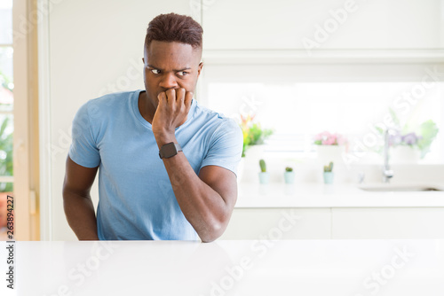 Handsome african american man wearing casual t-shirt at home looking stressed and nervous with hands on mouth biting nails. Anxiety problem.
