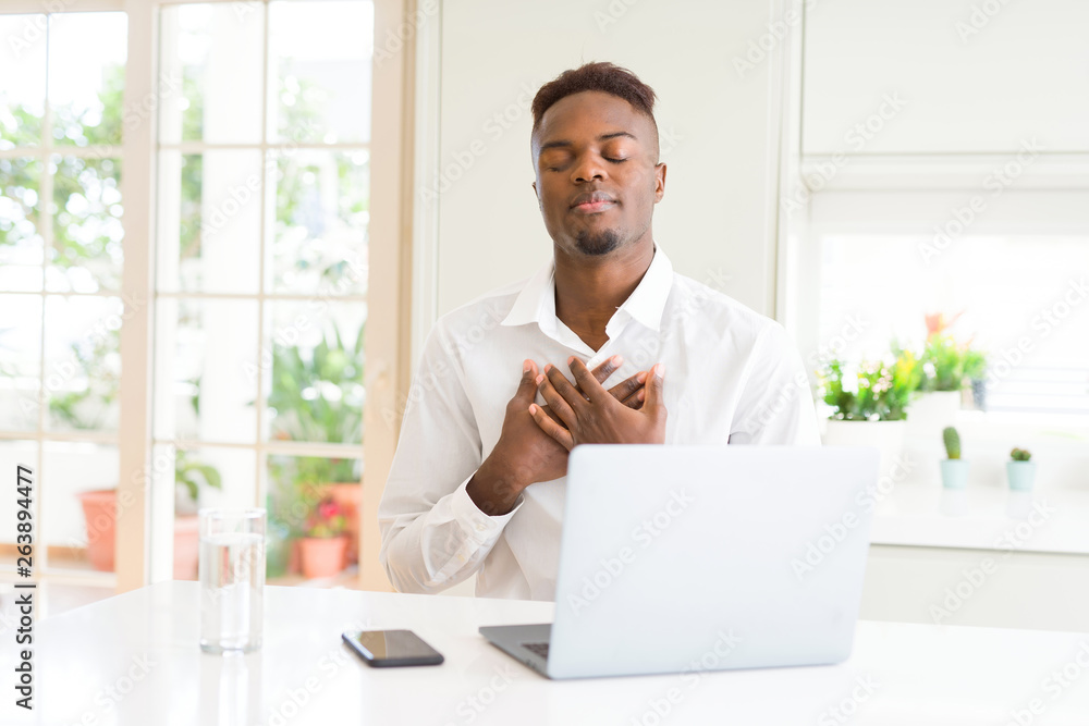 African american business man working using laptop smiling with hands on chest with closed eyes and grateful gesture on face. Health concept.