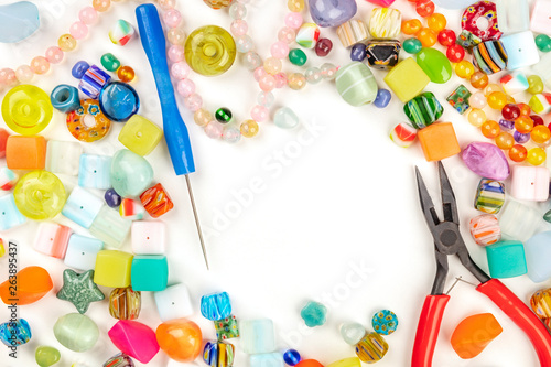 An overhead photo of many different beads with tools for making jewellery, on a white background with copy space