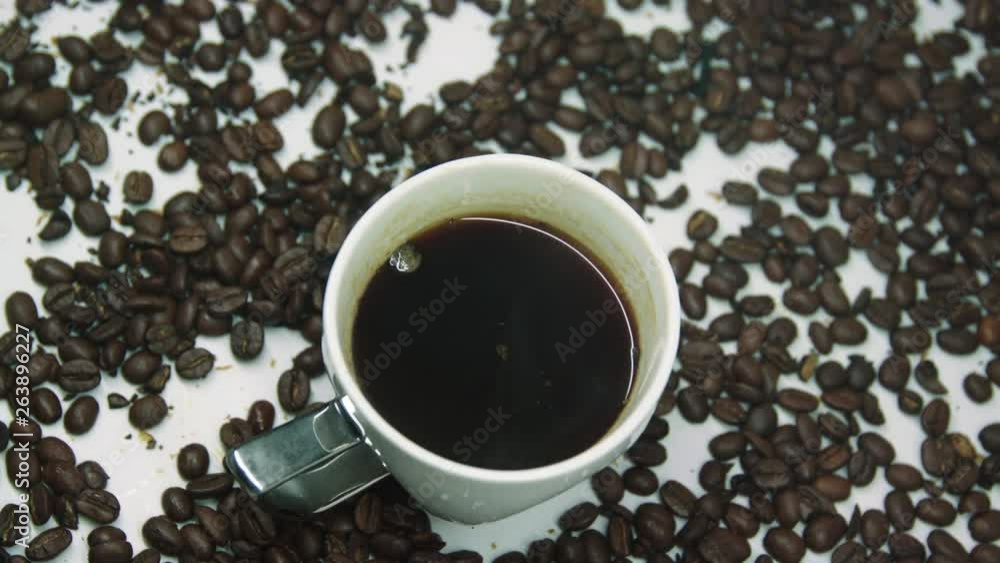 White hot cup of coffee with steam, surrounded by roasted coffee beans, rotating on a display turntable. White hot cup of coffee with steam, surrounded by roasted coffee beans, rotating on a display turntable.