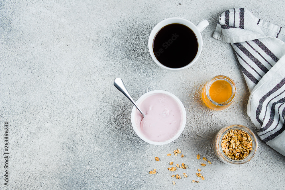 Healthy Breakfast Concept. Strawberry or raspberry yogurt, granola, honey and cup of coffee on light concrete table background. View from above with copy space. Flat lay Healthy Breakfast Concept. Strawberry or raspberry yogurt, granola, honey and cup of coffee on light concrete table background. View from above with copy space. Flat lay