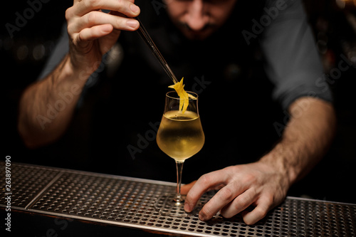Bartedner puts lemon rind with forceps in a cocktail