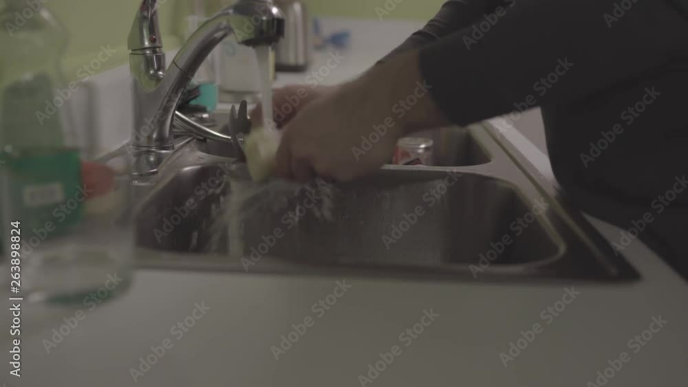Man washes the dishes by the sink, drying his hands and cleaning the counter in the kitchen. Man washes the dishes by the sink, drying his hands and cleaning the counter in the kitchen.