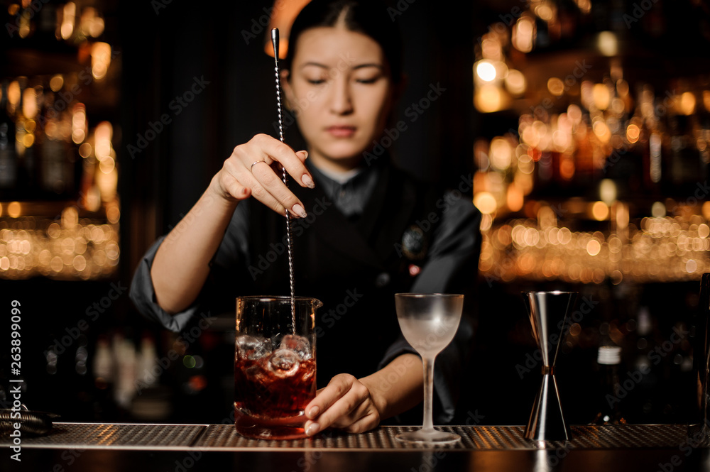Female bartender stirring alcohol cocktail with bar spoon