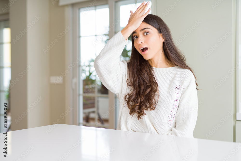 Young beautiful woman at home on white table surprised with hand on head for mistake, remember error. Forgot, bad memory concept. Young beautiful woman at home on white table surprised with hand on head for mistake, remember error. Forgot, bad memory concept.