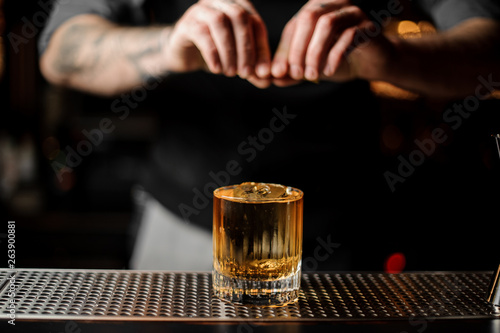 Bartender squeezes lemon rind in alcohol cocktail