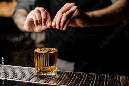 Bartender squeezes lemon rind in alcohol cocktail