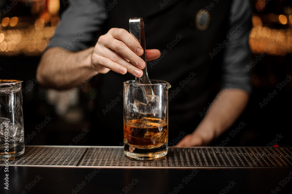 Bartender adding ice in glass with ice tongs