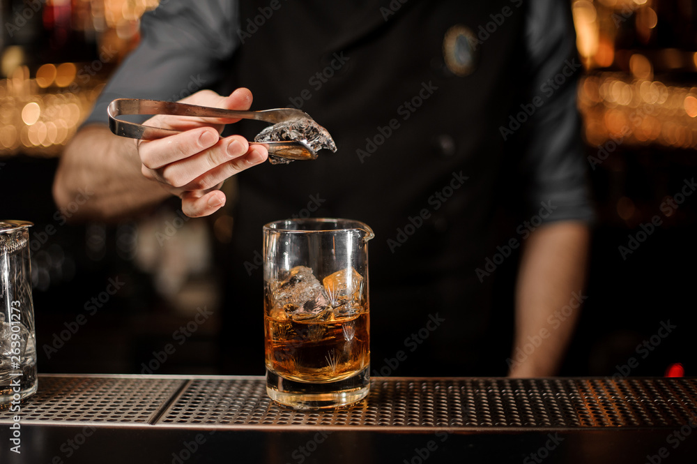 Bartender puts ice in glass with ice tongs