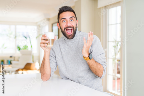 Handsome hispanic man drinking a cup of coffee very happy and excited, winner expression celebrating victory screaming with big smile and raised hands