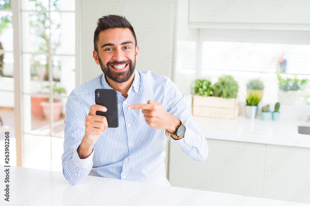 Handsome hispanic business man using smartphone very happy pointing with hand and finger