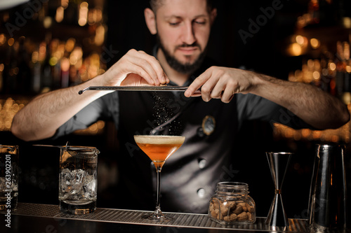 Bartender with beard pouring alcohol cocktail using grater