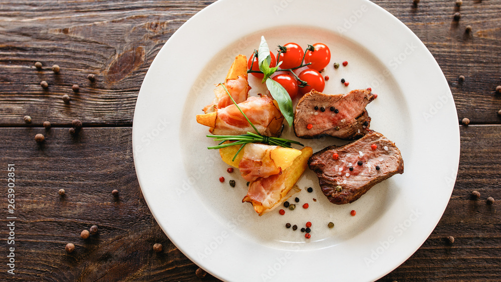 Restaurant catering business. Food presentation. Top view of roasted meat, baked potato with bacon and fresh cherry tomato. Restaurant catering business. Food presentation. Top view of roasted meat, baked potato with bacon and fresh cherry tomato.