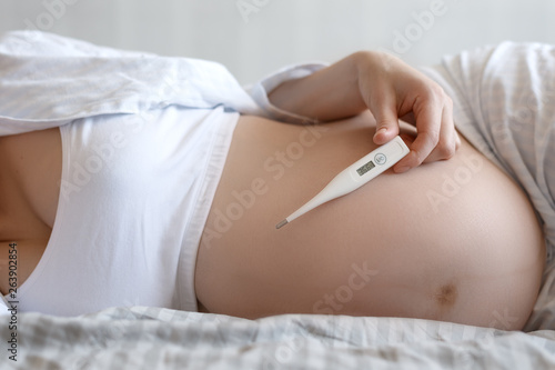 Close-up of the abdomen of a pregnant woman with an electronic thermometer in her hand. The concept of women's health during pregnancy