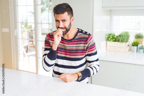 Handsome hispanic man wearing stripes sweater at home looking stressed and nervous with hands on mouth biting nails. Anxiety problem. © Krakenimages.com