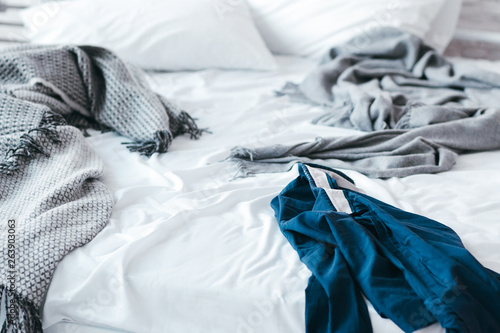 Messy habits and untidiness. Blue wrinkled shirt left in hurry on morning unmade bed with white sheets and gray blankets.