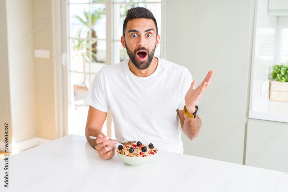 Handsome hispanic man eating healthy breakfast in the morning at home very happy and excited, winner expression celebrating victory screaming with big smile and raised hands Handsome hispanic man eating healthy breakfast in the morning at home very happy and excited, winner expression celebrating victory screaming with big smile and raised hands