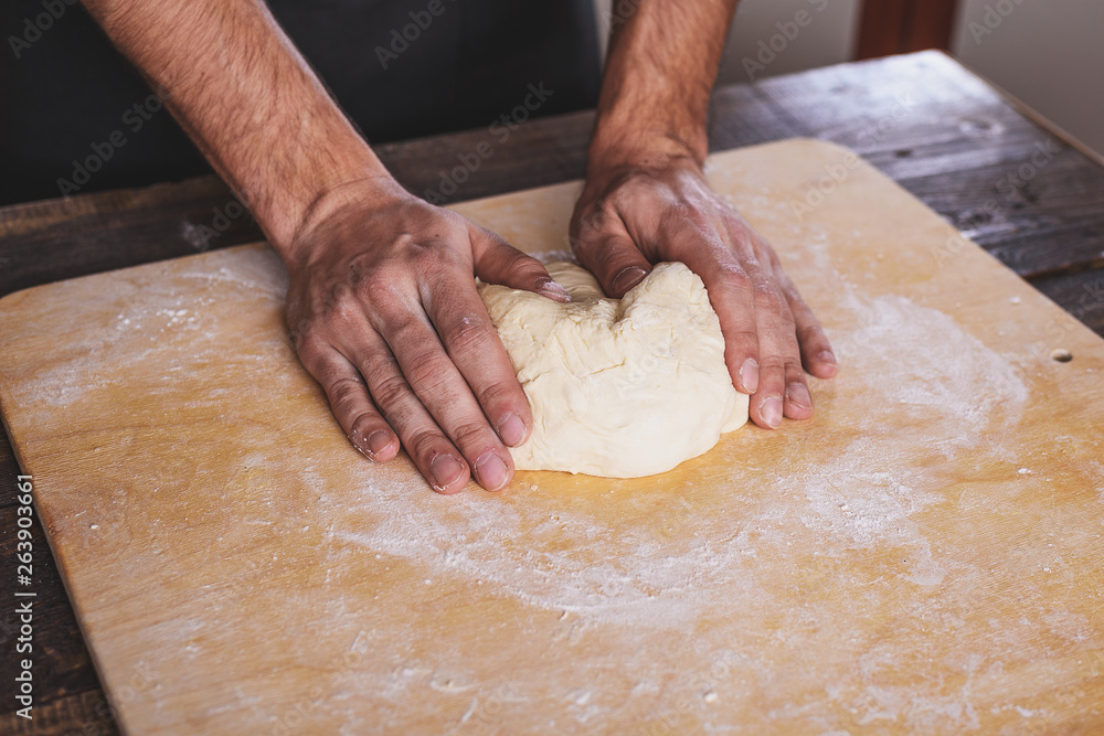 man kneads the dough in the kitchen