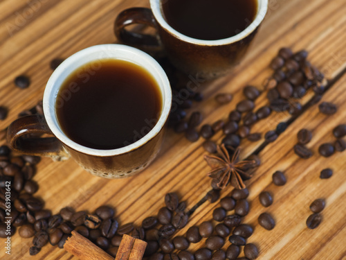Two small cups of freshly brewed espresso on a wooden background with scattered coffee beans