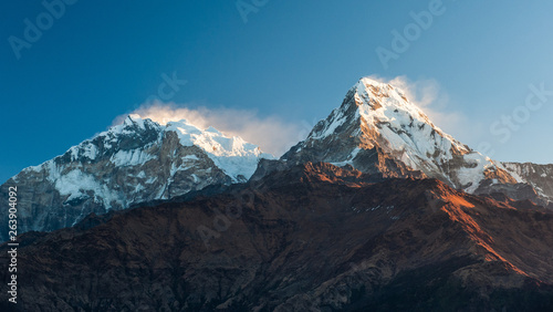 Poonhill view of Annapurnas. Warm pink and orange sunrise light over Annapurna mountain range with blue sky and beautiful clouds, view from Poon hill in Himalayas, Nepal. Annapurna one and Annapurna s