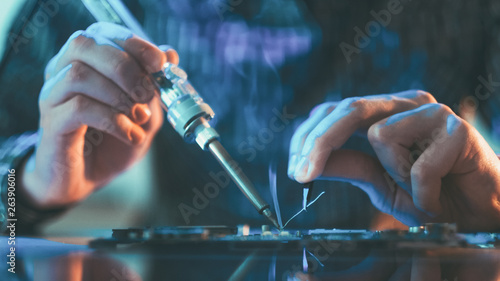 Electronic renovation in repair shop. Engineer working on circuit. Closeup of male hands soldering computer component. photo