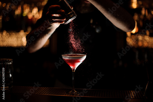 Male bartender sprinkles alcohol cocktail in a glass