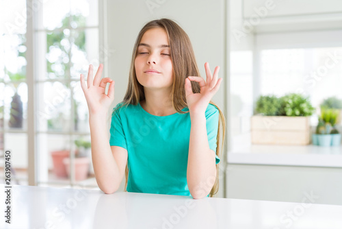 Beautiful young girl kid wearing green t-shirt relax and smiling with eyes closed doing meditation gesture with fingers. Yoga concept.
