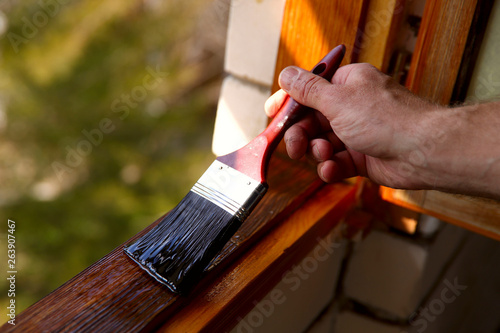 Fragment of a man's hand with a paint brush. A man paints a window with varnish. The concept of repair. Cropped shot, horizontal, close-up, place for text. Construction concept and hobby. photo