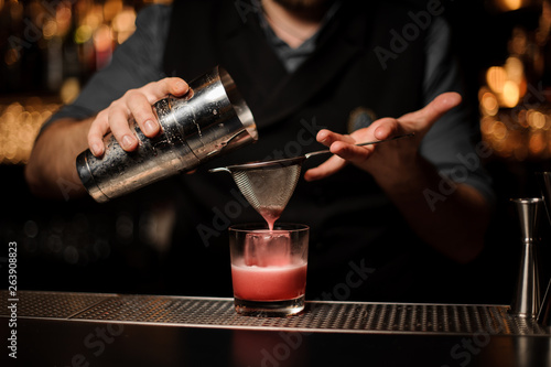 Close shot of bartender making cocktail with shaker and sieve