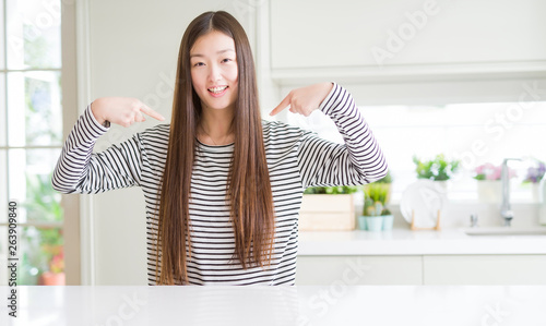 Beautiful Asian woman wearing stripes sweater looking confident with smile on face, pointing oneself with fingers proud and happy.