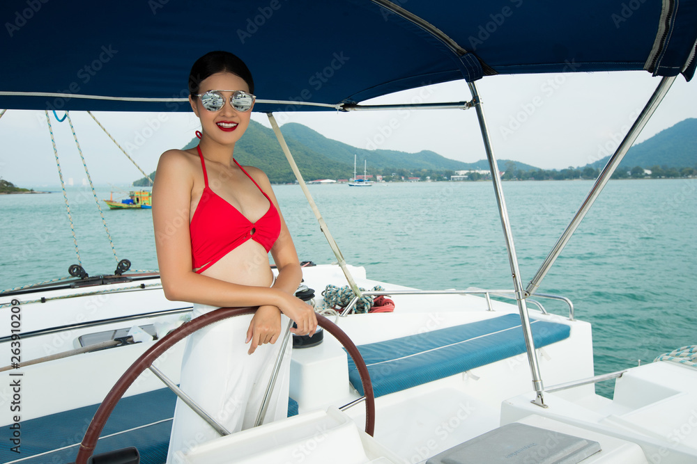 Beautiful Asian mix race Tanned skin Woman walk along Luxury Yachts in deep ocean, Red bikini sunglasses Girl posing as Fashion Model in docking pier under summer blue sky in vacation holiday