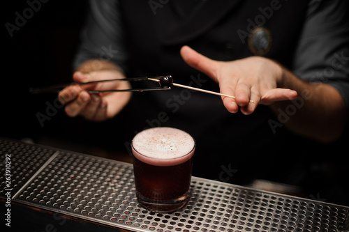Male bartender puts small cherry on toothpick with forceps