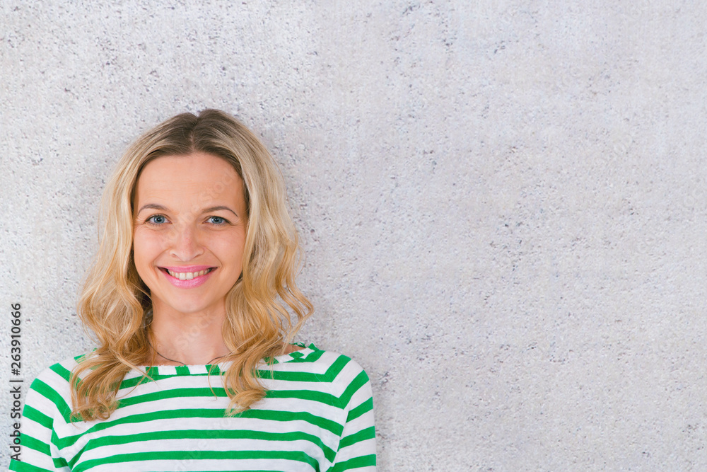 young, pretty blonde woman posing in front of a concrete wall and wearing green, white striped sweaters young, pretty blonde woman posing in front of a concrete wall and wearing green, white striped sweaters