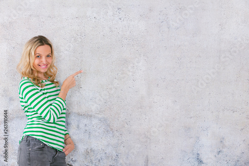young, pretty blonde woman posing in front of a concrete wall and wearing green, white striped sweaters