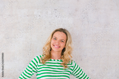 young, pretty blonde woman posing in front of a concrete wall and wearing green, white striped sweaters © epiximages