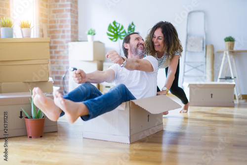 Middle age senior romantic couple having fun riding inside of cardboard, excited and smiling happy for moving to a new home