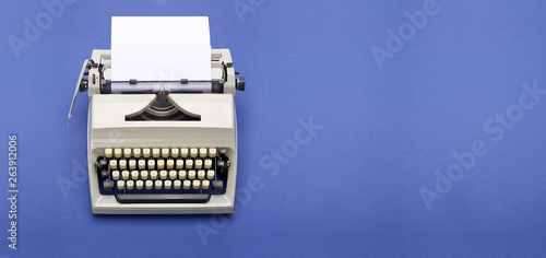 Top view of a typewriter from the 70s with blank paper for text, isolated on blue background.